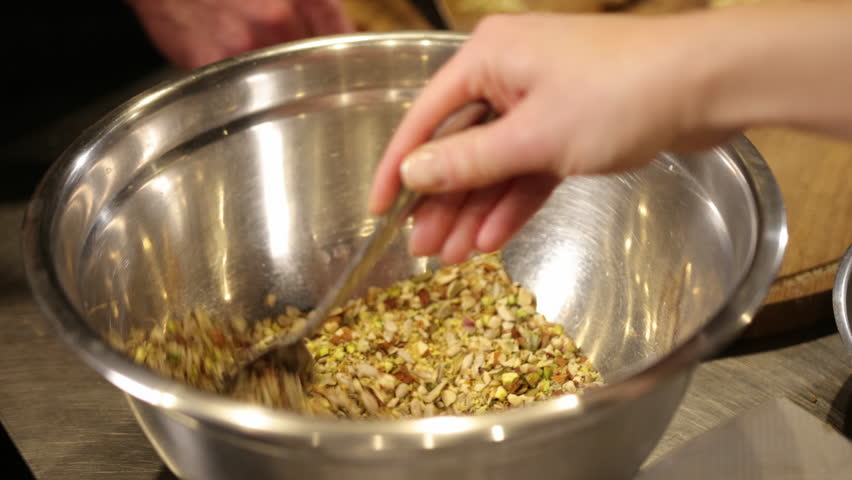 Hand stirring, healthy ingredients, mixing process. Close-up shot hand stirring mixture seeds and nuts in shiny stainless steel bowl. Mixing action suggests food preparation, focusing on healthy