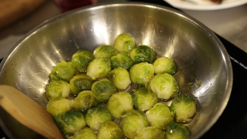Stirring spoon, kitchen setting, cooking veggies. Close-up captures Brussels sprouts being cooked in stainless pan, stirred by spoon held by hand, showcasing active and healthy cooking fresh produce.