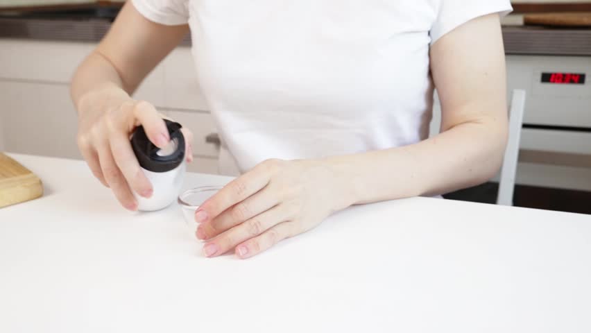 Woman pouring salt into a bowl, close-up of a grinder and salt, aromatic cooking in a modern kitchen. 