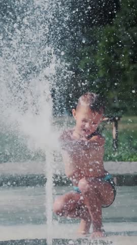 Boy having fun between water jets, in fountain, run around, sprinkle, have fun, have fun, on a hot summer day.
