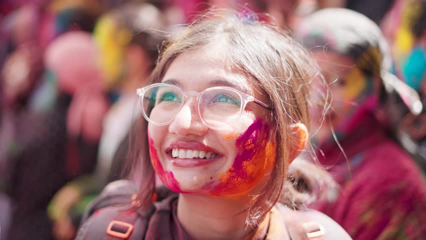 4K portrait of Indian girl smiling and her face covered with powdered colors during Holi Festival in Sangla, Himachal Pradesh, India. Hindu woman celebrating. Tourists seeking cultural experiences.