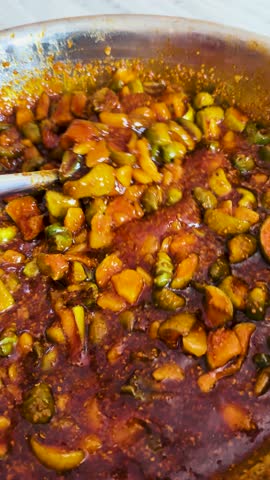 4K Vertical shot of Mixing spices with homemade pickle. Mango and glue berry pickle. Female preparing food in kitchen. An Indian housewife.