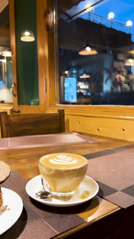 4K Vertical shot of Cappuccino and fresh Carrot cake on cafe table during evening at Manali, Himachal Pradesh, India. Tourist enjoying food in authentic restaurant. Coffee on table.