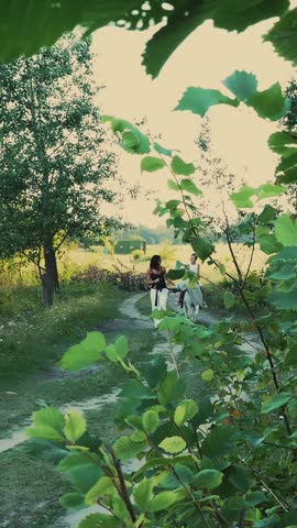 Son is riding a pony, mother is holding a pony for a bridle. Cheerful, happy family vacation. Outdoors, in summer, near the forest. A woman and a boy are walking around the field