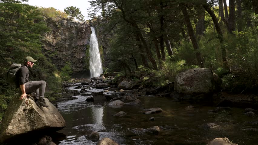 Hiker sitting on a rock overlooking waterfall pulling dirt out of his shoe. Outdoors pursuit concept