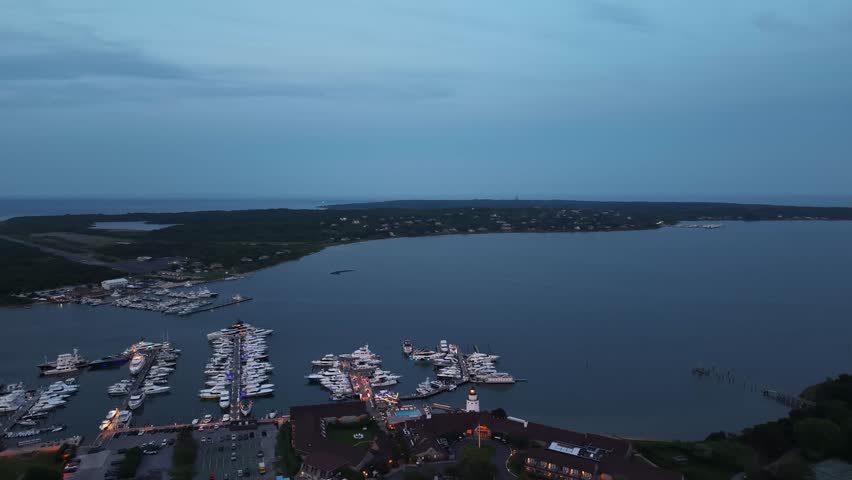Darker aerial shot of a yacht club and surrounding Lake Montauk with open ocean in the background. Stunning aerial view from high above. 4K footage of night falling on the yachts. East end Long Island