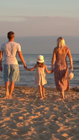 Back view of happy family walk on sand beach at sea at sunset. Father mother and little daughter on summer vacation.Travel holiday. Vertical shot