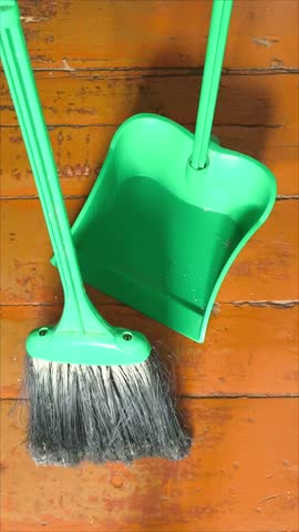 A broom sweeps the trash from the wooden floor into a plastic dustpan. House cleaning. Crumbs, small debris on the floor.