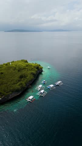 Moored Outrigger Bangka Boats Against a Dramatic Limestone Shoreline in sunny paradise Pescador Island  – Moalboal, Cebu, Philippines