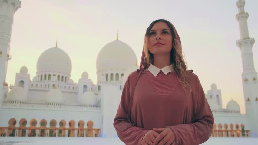 European women tourist admires modern Arabian architecture. Beautiful white marble building Muslim temple, mosque. Yellow blue illumination image flowers floor. long pink abaya dress. Abu Dhabi UAE 4k