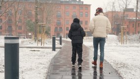 Two brothers walk away from the camera on a city sidewalk during a winter snowfall. The younger sibling shows support for the older one, symbolizing a family connection, trust, and friendship. - Powered by Shutterstock - Get 15% off with code: PIKWIZARD15