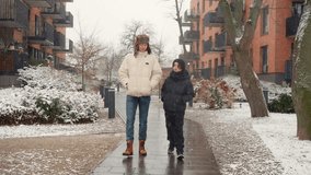 Two sibling brothers walk towards the camera on a sidewalk in a residential district during a winter snowfall. Teenagers walk together, enjoying a calm outdoor activity in cold weather. - Powered by Shutterstock - Get 15% off with code: PIKWIZARD15