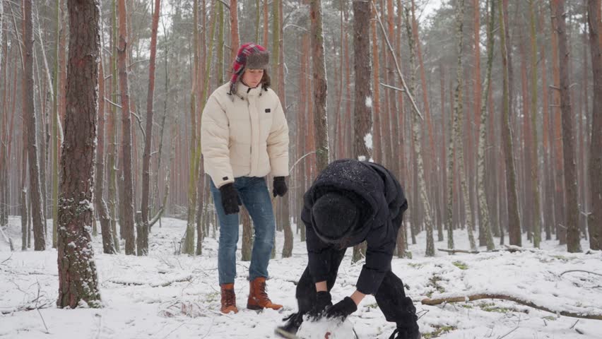 Two brothers start a new project in a winter forest, laying the foundation for a snowman. This is the initial stage of a joint effort, where small beginnings can grow into a big result.