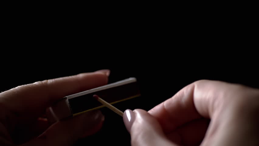 Lighting Match on Matchbox in Dark Room. Female hands lighting and striking match. Burning match, sparks, clouds of thick smoke. Room lighting. Power outage. Slow motion. Close-up.
