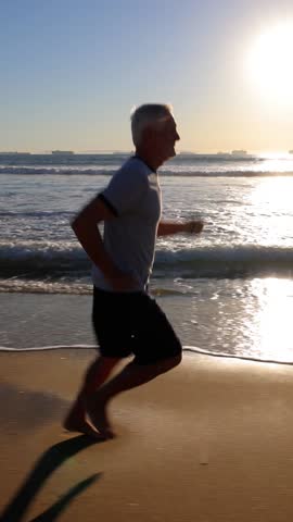 64 year old man getting his exercise at the beach at sunset. Vertical Video.