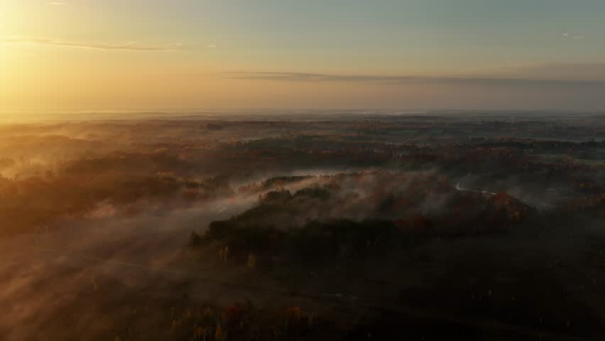 Beautiful dawn aerial shot of sunlight shining thought the trees and low fog in Minnesota in the autumn. Trees are turning their fall colors
