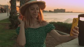 Woman tourist wear green dress, sunglasses and sunhat  smiling while making video call with smartphone in park near beach at sunset. Travel, blogging, weekend, relax and lifestyle concept  - Powered by Shutterstock - Get 15% off with code: PIKWIZARD15