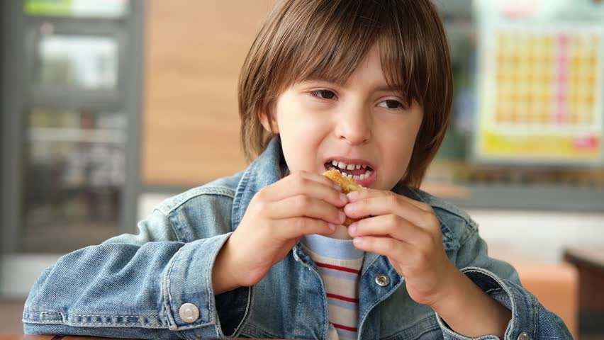 Little boy is eating chicken nuggets in fast food Restaurant or cafe