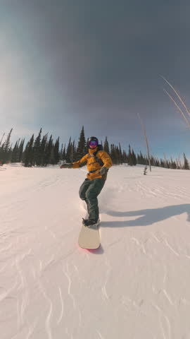 Vertical video, Snowboarder rushes between trees in high-speed freeride session. Clear cold day, white slope, and healthy sport motion reflect mountain lifestyle and winter adrenaline in natural snowy