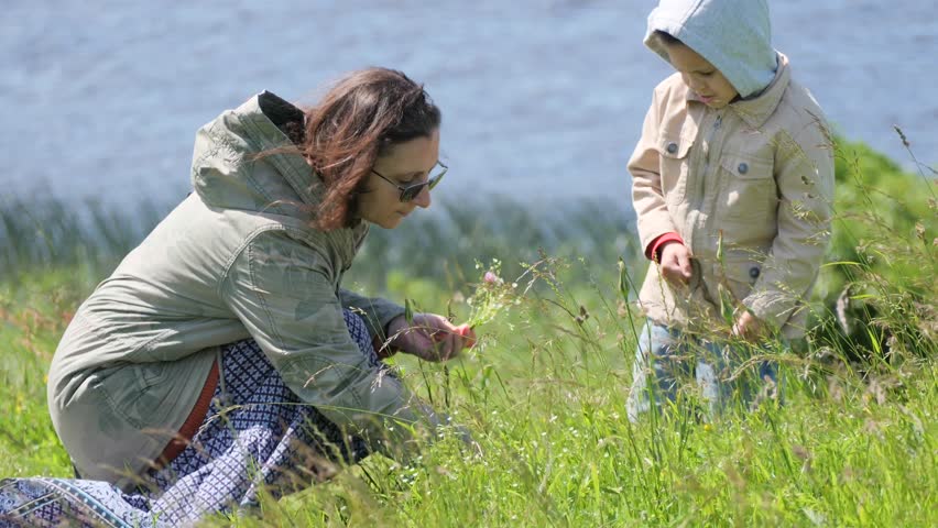 Mother and Child Bond in Sunny Green Field Picking Wildflowers by River - Family Nature Outdoors