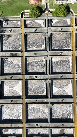 Vertical aerial video of activated sludge tanks at a wastewater treatment facility. Direct top-down drone shot showing industrial sanitation process and tanks