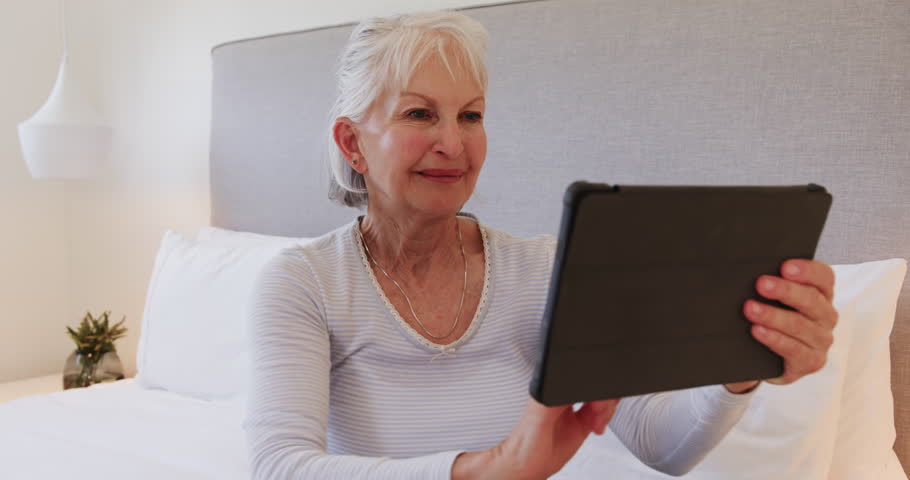 Senior woman relaxing on bed, using tablet for reading at home. Technology, retirement, lifestyle, digital, leisure, relaxation