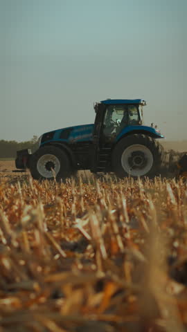 A tractor works diligently on a dusty field during the afternoon in the countryside, preparing the land for future crops. The sun casts a warm light on the hard-working machine