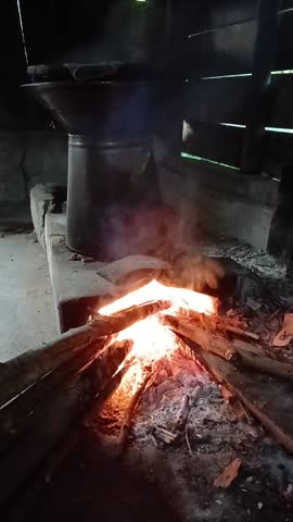 Documentary-style video of traditional food preparation in a rural Indonesian home. A woman is preparing opak over open flames using a simple stove setup.