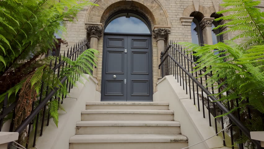 Approaching a black front door to a townhouse or home with stairs and metal railings.