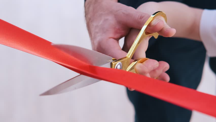 Close-up of golden scissors as an adult and a child cut a red ribbon together, symbolizing a meaningful moment, intergenerational unity, and the ceremonial nature of the event
