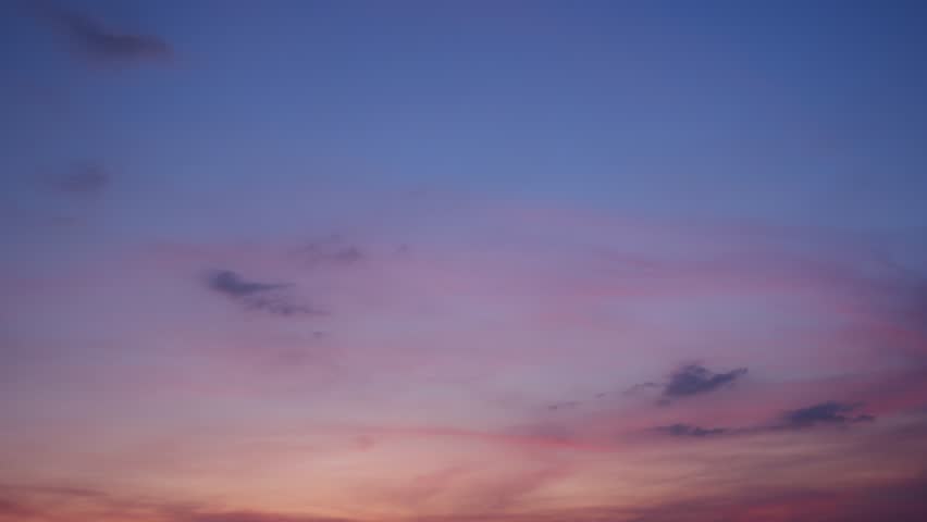 A captivating sunrise sky timelapse with soft pink and purple clouds glowing gently against a fading dark blue sky, evoking a peaceful and hopeful start to the day as light slowly spreads. Time-lapse.