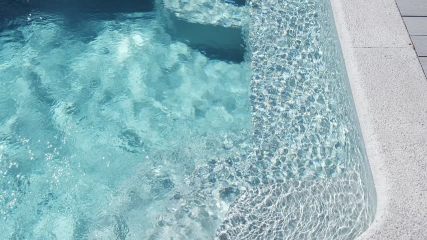 Clear blue water in a private outdoor pool with mosaic tiles and soft sunlight reflections on the surface creates a refreshing, cozy atmosphere of summer relaxation
