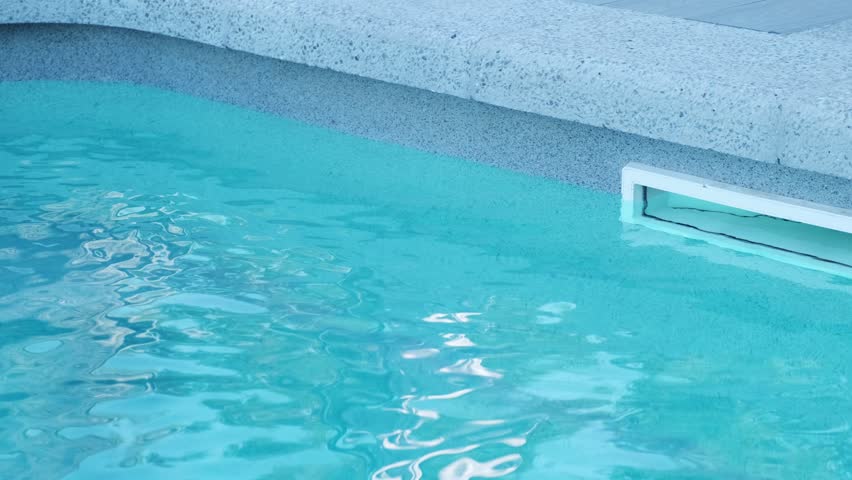 Section of a swimming pool edge with a skimmer for water filtration. The blue water reflects daylight, creating a sense of cleanliness and comfort. Modern materials emphasize a neat design
