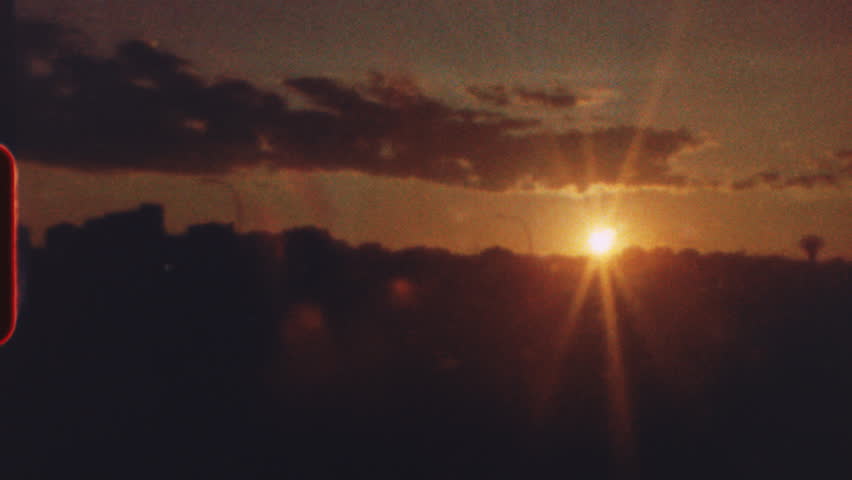 8 mm film - vibrant orange and yellow sunset casting warm glow over metropolitan skyline, featuring nostalgic light leak effect creating vintage aesthetic and serene urban atmosphere