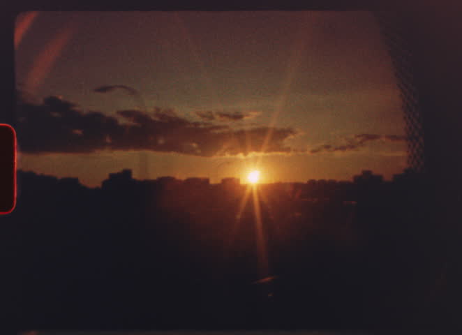 8 mm film - warm golden sunset illuminating urban skyline, vibrant orange hues spreading across cloudy sky during twilight transition