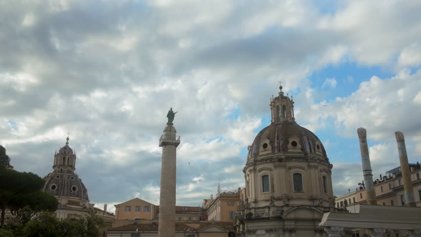 Low angle view of domed churches and Trajan’s Column under a dramatic cloudy sky in the heart of historic Rome