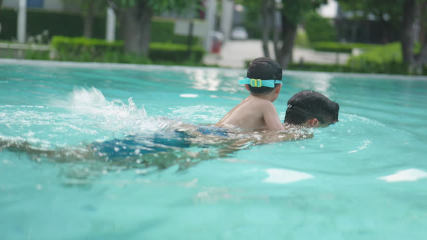 Asian boy joyfully rides on his father’s back in the swimming pool.4k
