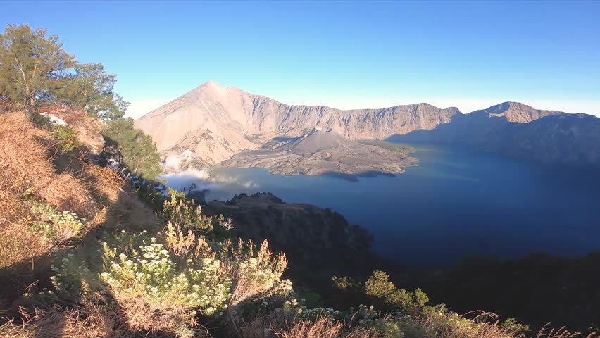 Dramatic footage of a small newly formed volcano in Bali, Indonesia, emitting smoke and steam into the sky. Surrounded by lush tropical vegetation and volcanic terrain, the scene captures the raw powe