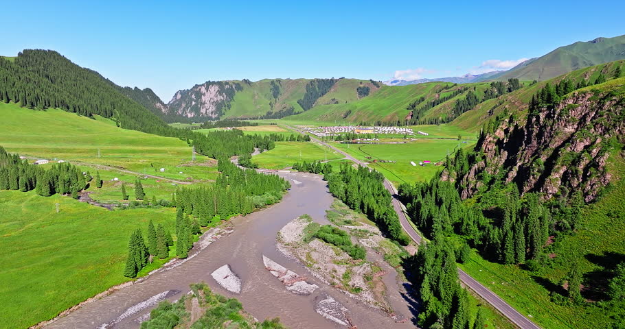 Aerial shot of winding river and road through green valley in summer. Beautiful grassland nature landscape in Xinjiang, China.