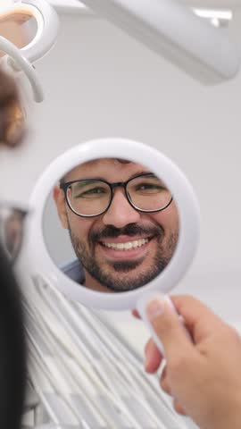 Joyful patient smiling while looking in mirror during dental visit. Vertical video.