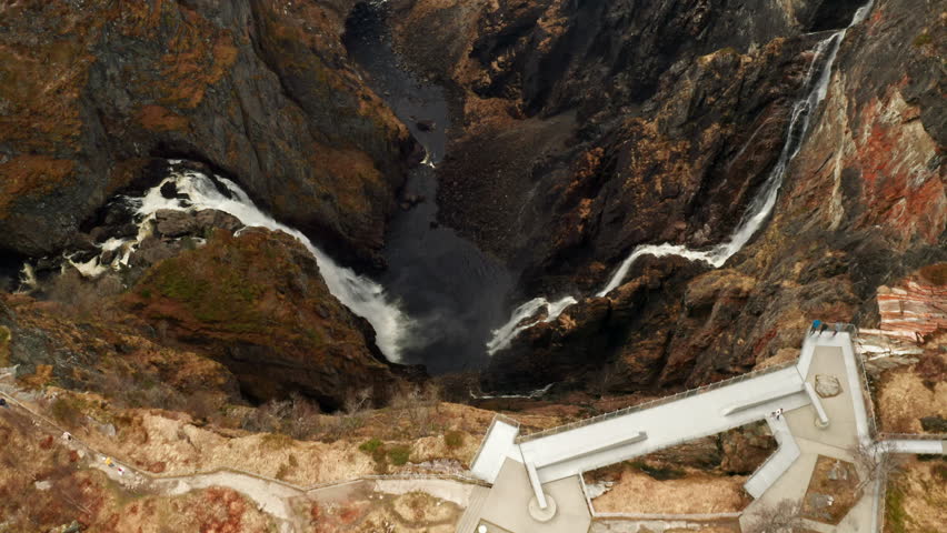 Deep valley of Voringsfossen waterfall area carved by winding river snaking through rocky landscape. Steep slopes marked by hints of sparse vegetation