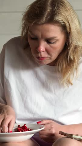 A hungry woman in a white T-shirt greedily eats strawberries with her hands, picking up a handful of berries. A pregnant woman's whim. Eating behavior eating food quickly