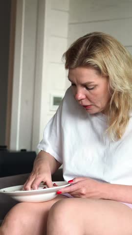 A hungry woman in a white T-shirt greedily eats strawberries with her hands, picking up a handful of berries. A pregnant woman's whim. Eating behavior eating food quickly