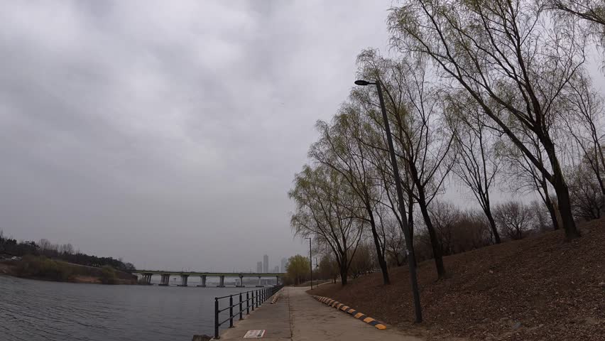 Walkway At Riverside Park With Bare Trees With Yanghwa Bridge In Distance. Han River In Seoul, South Korea. wide POV shot
