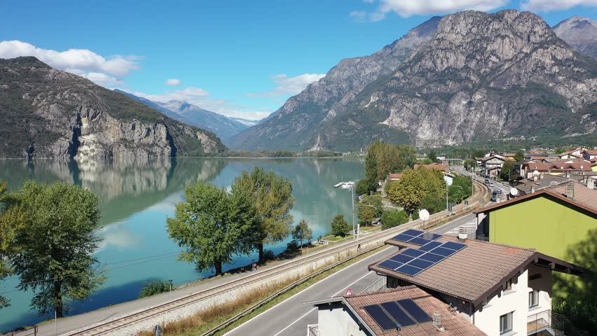 On a beautiful sunny day in Verceia village, a train of Trenord Railway dashing along Lago di Mezzola, which is nestled under majestic alpine mountains north to Lake Como, in Lombardy, northern Italy