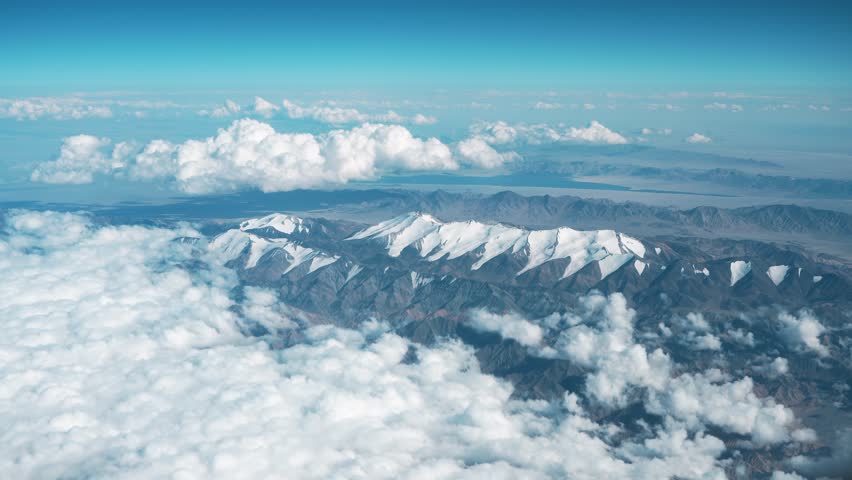 Snow-Capped Mountain Range Seen from Airplane Window Above the Clouds. Aerial View of Bogda Peak in the Tian Shan Mountains.