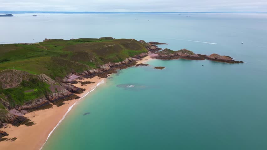 Aerial drone view of the idyllic Plage de Lourtuais beach, the rocky peninsula of Cap d'Erquy, and calm turquoise sea in Brittany, France