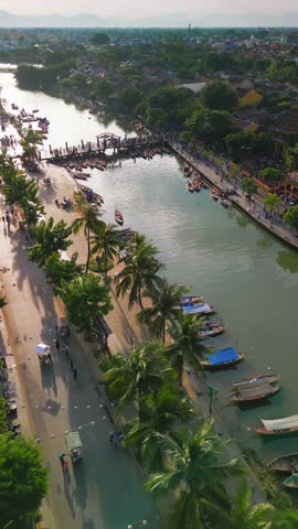 Bright vertical aerial footage of boats moored along the Hoi An riverbank, Vietnam. High quality concept video for travel, tourism, culture, and scenic city lifestyle promotions.