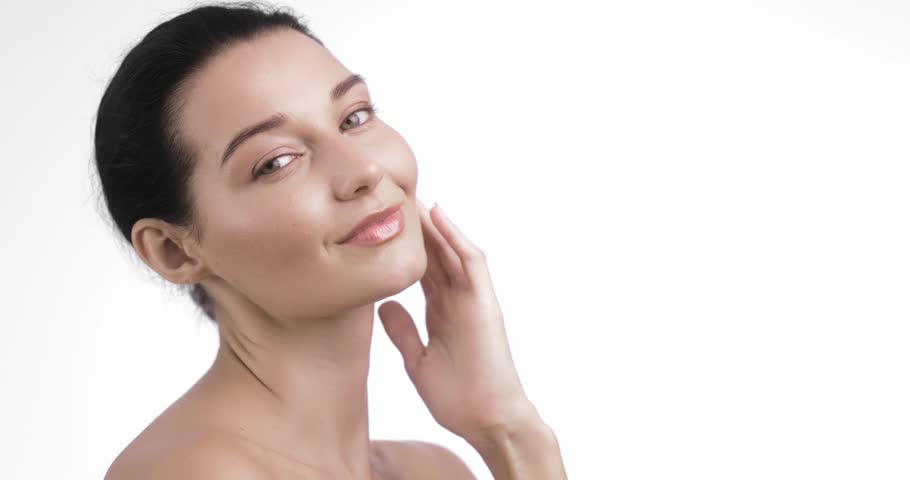 Confident young woman smiles and caresses shoulder while tilting her head in a soft, minimalist frame. Perfect for beauty tutorials, skincare branding, and peaceful lifestyle promos.