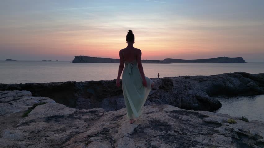 Yoga Hippie Girl at sunset with island in the background, Ibiza, Spain. Majestic aerial view flight ascending drone